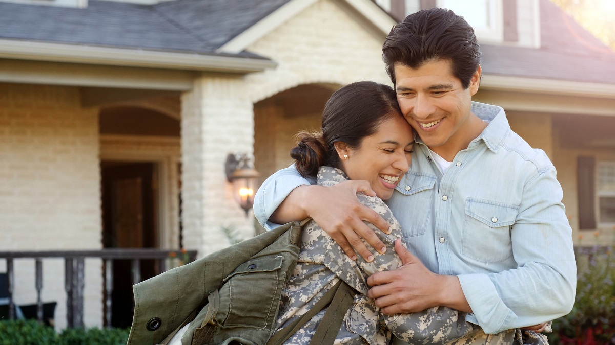 Couple hugging in front of their home. 